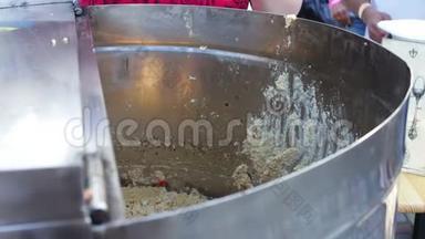 一个女人`手把粥从一个大缸里倒进一个塑料盘子里。 街头美食，快餐，街头小吃，美味